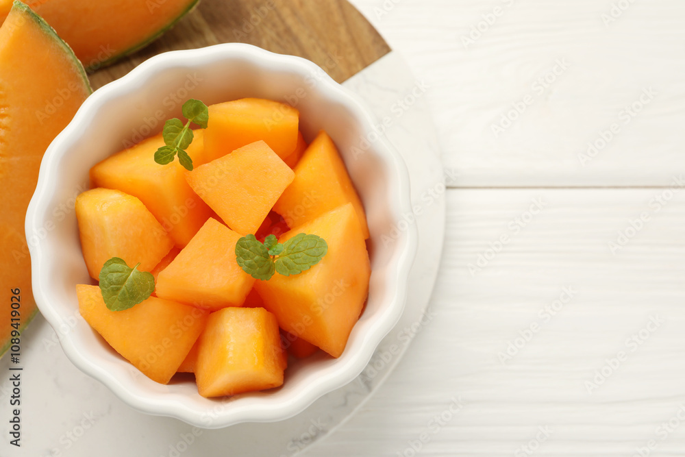 Pieces of Cantaloupe melon and mint in bowl on white wooden table, top view. Space for text Pieces of Cantaloupe melon and mint in bowl on white wooden table, top view. Space for text