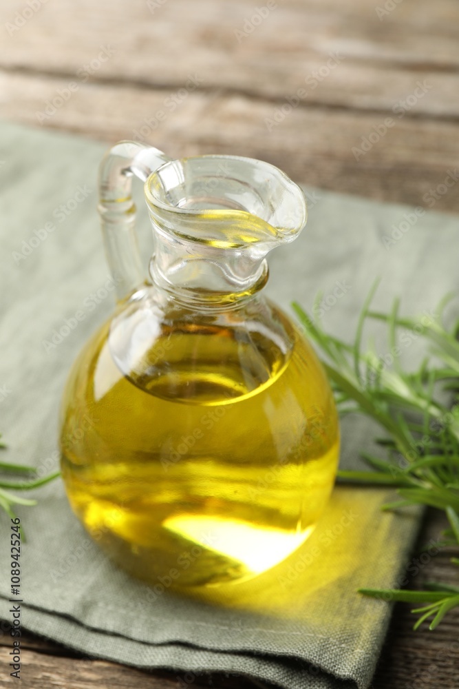 Cooking oil in jug and rosemary on wooden table, closeup Cooking oil in jug and rosemary on wooden table, closeup