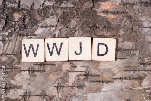 Christian religious background concept. WWJD (What Would Jesus Do) written with wooden block letters on natural wood bark background. 