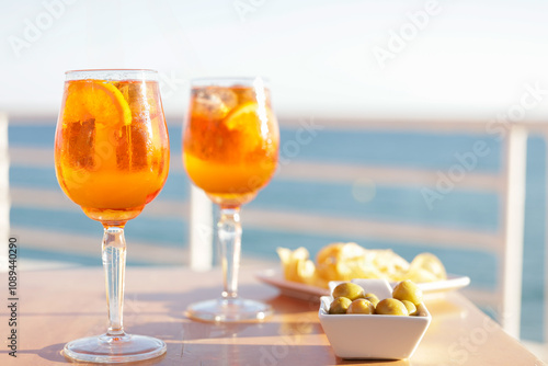 Aperol spritz cocktail glasses with olives and potatoes chips aperitif, very Mediterranean. Sea views, gastronomy and travel concept.