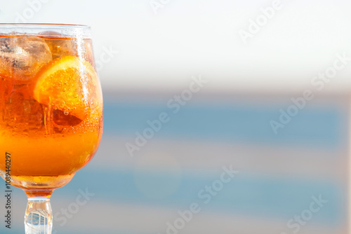 Closeup of an Aperol spritz cocktail glass. Sea views, gastronomy and travel concept.