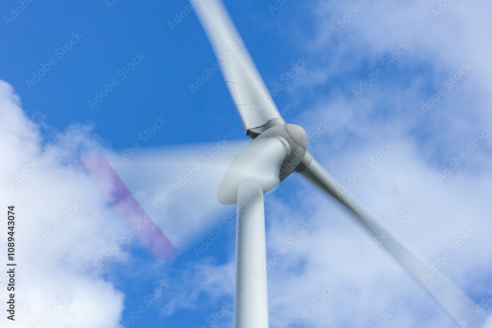 Windrad in Bewegung mit Bewegungsunschärfe vor blauem Himmel mit Wolken Windrad in Bewegung mit Bewegungsunschärfe vor blauem Himmel mit Wolken