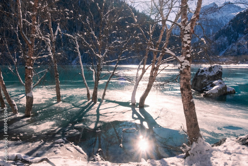 A beautiful winter lake in the mountains, surrounded by a spruce forest, has already frozen over on a sunny and frosty day. Lake Issyk Almaty Kazakhstan.