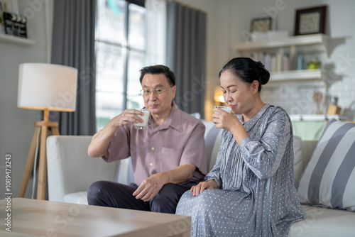 An elderly couple enjoys a peaceful moment at home, sharing smiles and drinks. The warm and cozy atmosphere emphasizes their deep connection, happiness, and the comfort of spending time together.