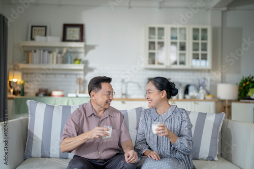 An elderly couple enjoys a peaceful moment at home, sharing smiles and drinks. The warm and cozy atmosphere emphasizes their deep connection, happiness, and the comfort of spending time together.