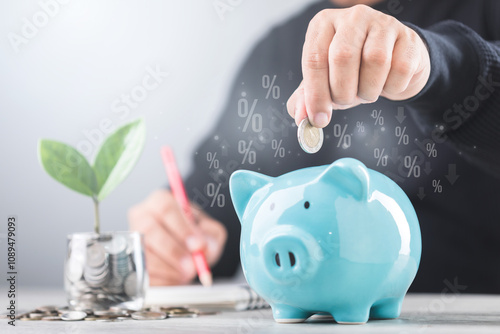 Businessman drops a coin into a blue piggy bank, Coin jar with a small seedling growing in the center. He writes numbers in a notebook, symbolizing saving, growth, and careful financial planning