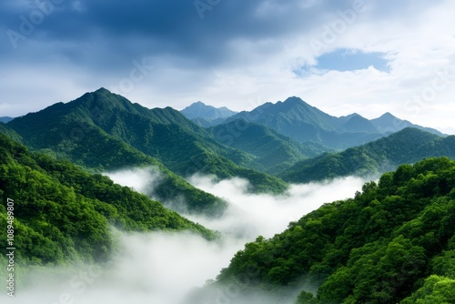  a view of a mountain range from the top of a hill, with lush green trees on the hills and a sky filled with clouds in the background