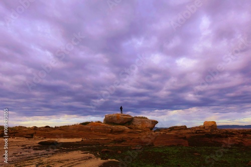 Paisaje de hombre subido a una roca bajo un cielo de nubes oscuras.  photo