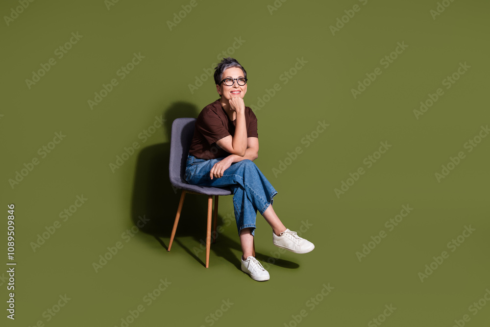 Full size photo of lovely pensioner lady sit chair look minded empty space dressed stylish brown garment isolated on khaki color background Full size photo of lovely pensioner lady sit chair look minded empty space dressed stylish brown garment isolated on khaki color background