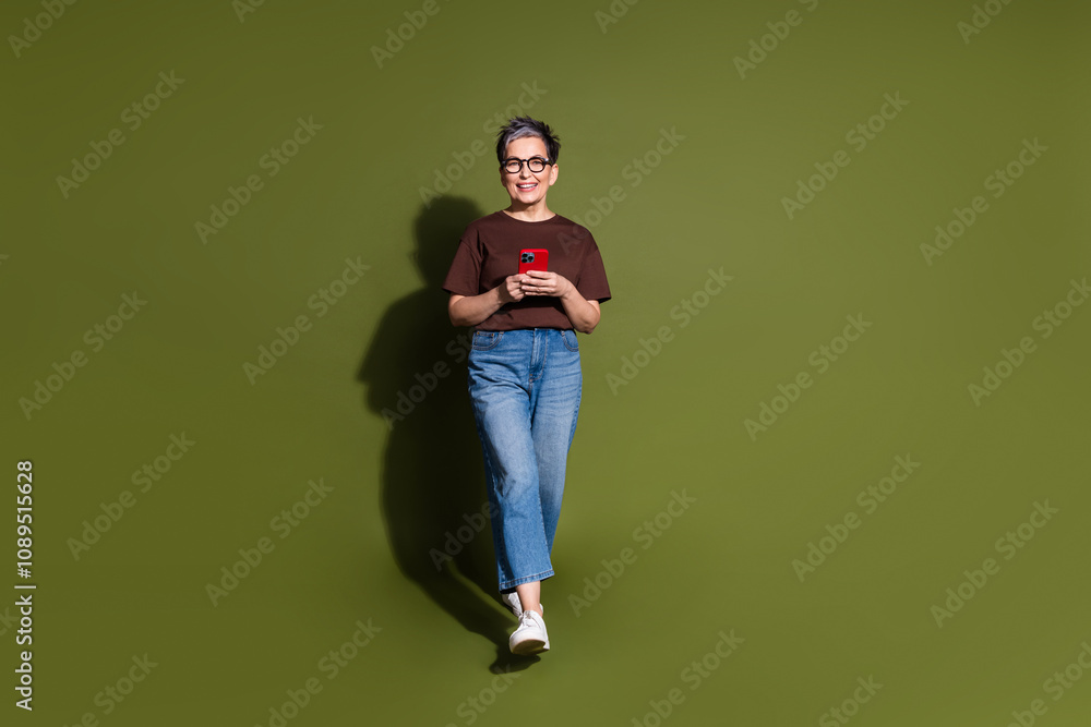 Full body portrait of pretty aged lady walk smart phone wear t-shirt isolated on khaki color background Full body portrait of pretty aged lady walk smart phone wear t-shirt isolated on khaki color background