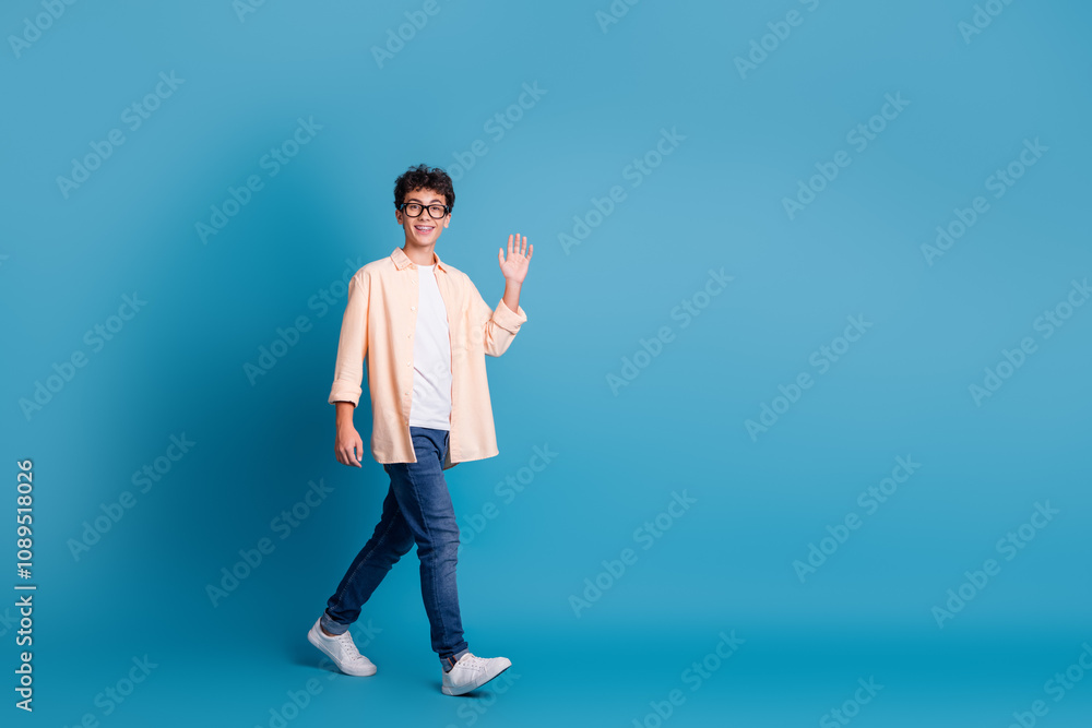 Joyful young man in casual attire against blue background waving, embodying modern youth and vibrant lifestyle Joyful young man in casual attire against blue background waving, embodying modern youth and vibrant lifestyle