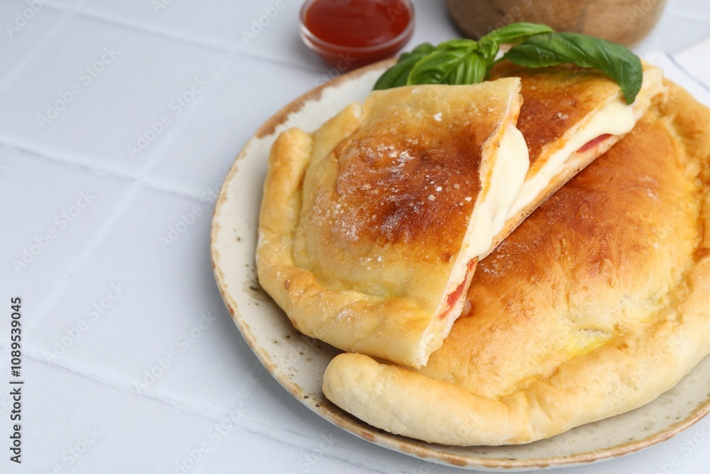 Pieces of delicious calzone pizza with mozzarella, tomatoes and basil on white tiled table, closeup Pieces of delicious calzone pizza with mozzarella, tomatoes and basil on white tiled table, closeup