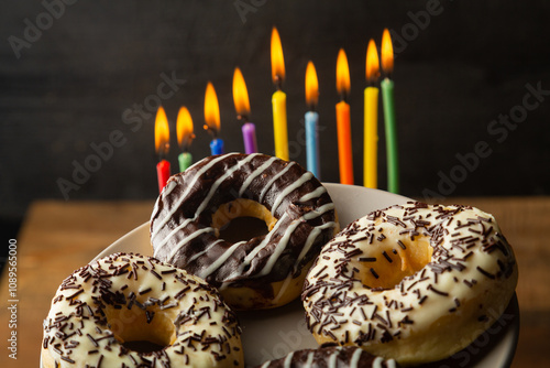 Hanukkiah with colored candles on the table and donuts in chocolate glaze photo