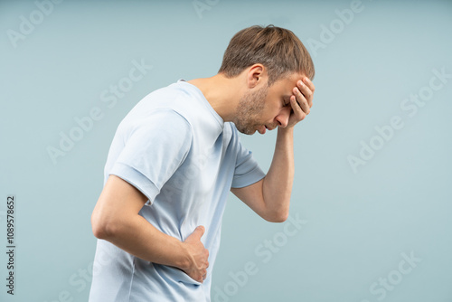 Photos Weary crouched man holds forehead, stomach struggling with dizziness, nausea feels symptoms of high blood pressure by stress, fatigue, food poisoning dehydration