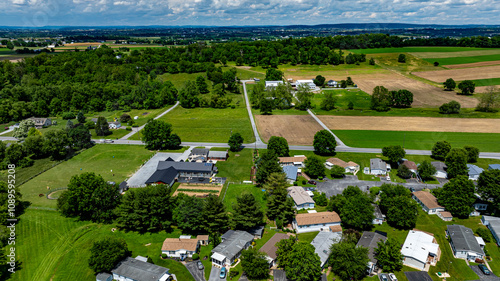 Aerial view of a tranquil rural community featuring various Mobile, Prefab, Manufactured houses situated near lush green fields and trees. The landscape shows harmonious blend of residences farmland.