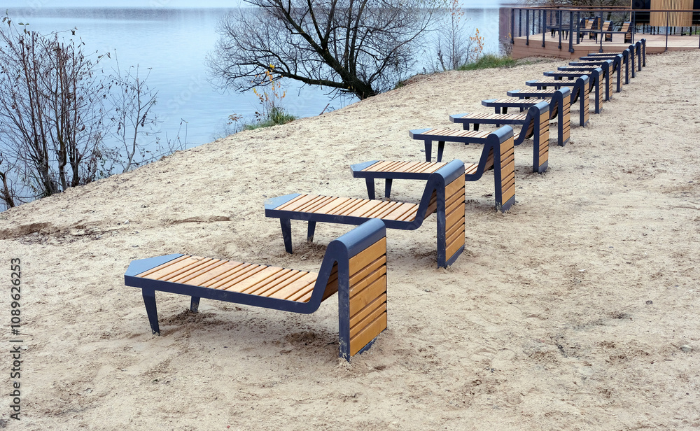 Sandy beach with many empty wooden sun chaise loungers and chairs near the river at the end of summer season Sandy beach with many empty wooden sun chaise loungers and chairs near the river at the end of summer season