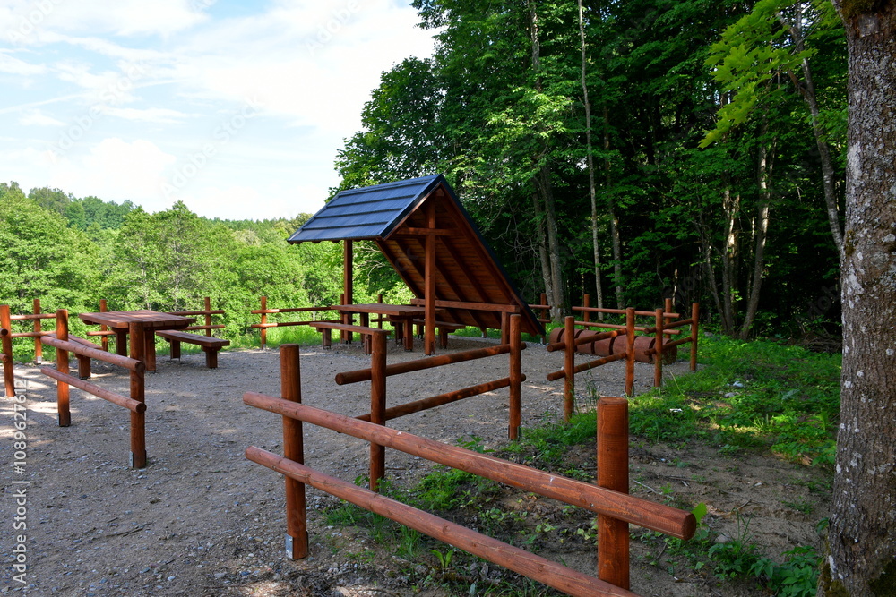 A view of a wooden shack, shelter, or hut made out of timber and having a slanted, tiled roof located next to a lush forest or moor and a wooden fence surrounding a paddock or yard of sorts A view of a wooden shack, shelter, or hut made out of timber and having a slanted, tiled roof located next to a lush forest or moor and a wooden fence surrounding a paddock or yard of sorts