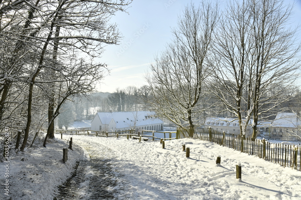 Fototapeta premium Chemin à pavés descendant vers le domaine de l'abbaye du Rouge-Cloître sous la neige à Auderghem 