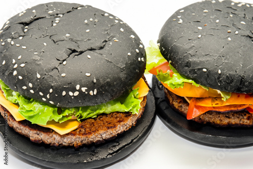 Two black hamburgers with cheese and lettuce. A hamburger with a black and gray background. Black hamburger gray background fast food buns. A hamburger with black buns on a gray lifestyle background. photo