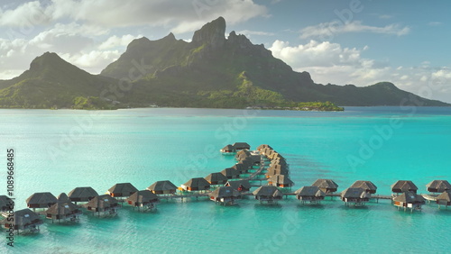 Aerial view overwater bungalows forming line towards mount Otemanu on tropical exotic Bora Bora island, with its turquoise lagoon and lush vegetation. Luxury travel vacation resort in coral reef ocean