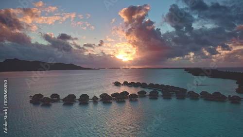 Overwater bungalows in Bora Bora colorful sunset, warm glow on turquoise water, dramatic colorful clouds sky background. Popular tourist destination. Remote wild nature paradise, exotic summer travel