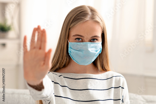 No contacts. Young woman in medical protective mask gesturing stop at home photo