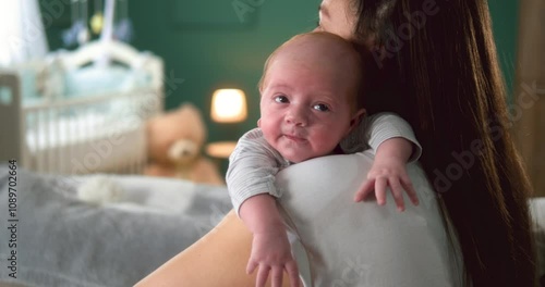Mother holding baby infant on shoulder and tapping back to belch after feeding 