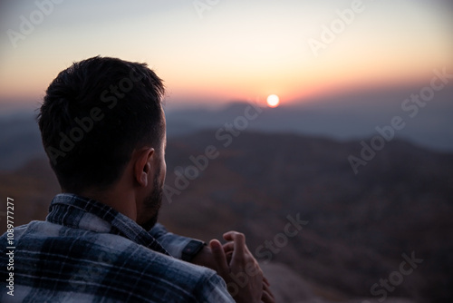 A young man looks at his watch at sunset.