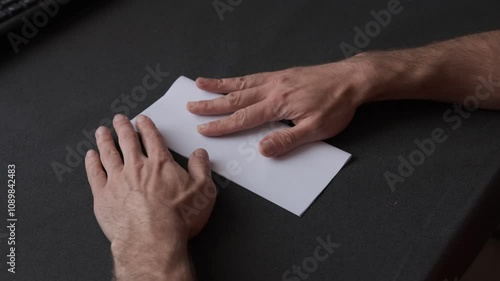 Hands folding a white sheet of paper on a black surface, creating an intricate origami figure in slow motion