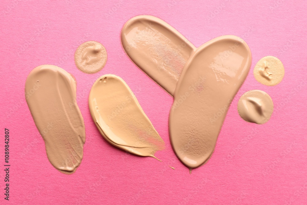 Fototapeta premium Foundation on pink background, top view. Smears of cosmetic product