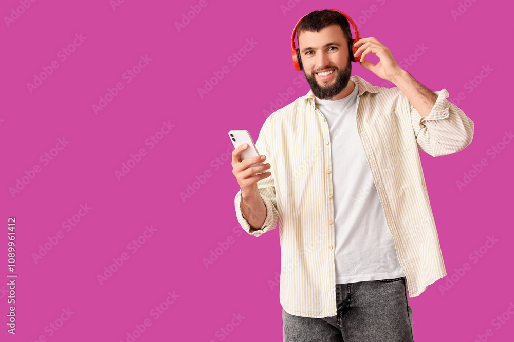 Fototapeta premium Handsome young happy man in headphones with mobile phone on purple background