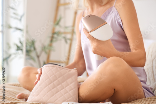 Mature woman with photoepilator and bag sitting in bedroom, closeup photo