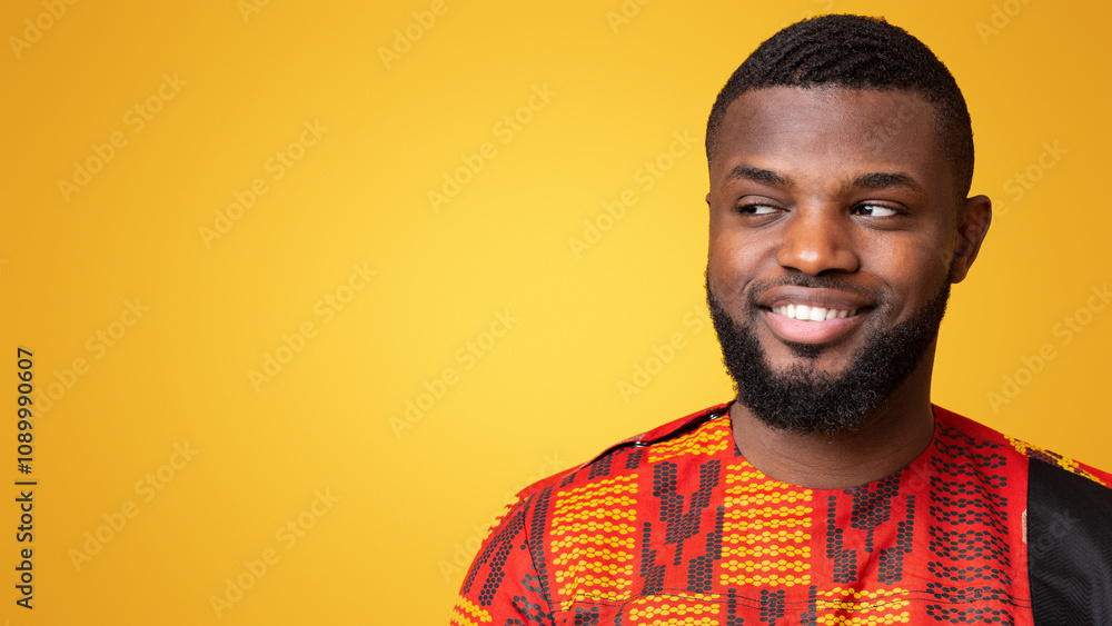 Obraz premium Interested black guy smiling and looking at free space, yellow studio background, panorama