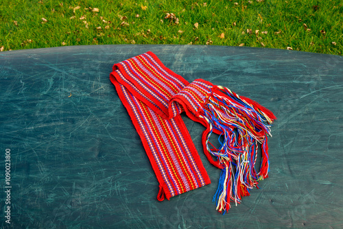 ceinture fléchée (traditional pattern) replica of the woven sash worn by voyageurs during the fur trade on overturned green canoe  room for text