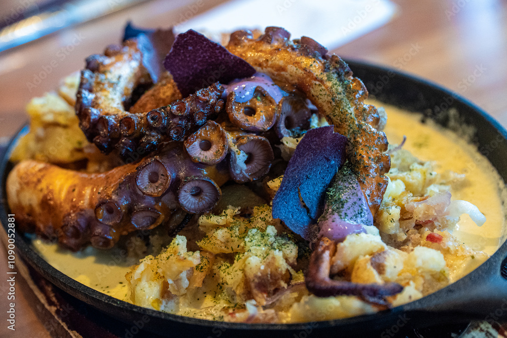 A gourmet presentation of tender octopus paired with golden potatoes, served on a ceramic plate in an elegant restaurant setting