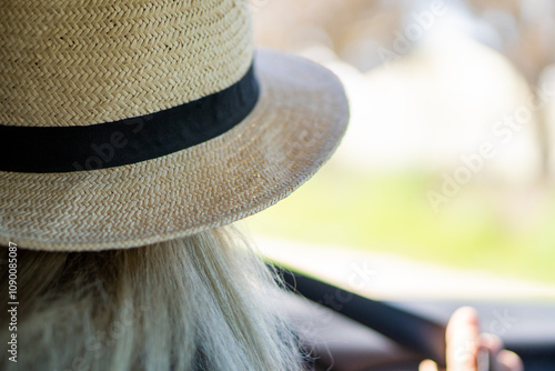 Woman wearing a woven straw hat with a black ribbon, basking in soft sunlight while driving
