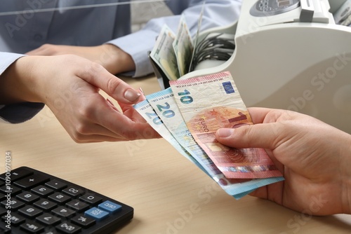 Client giving euro banknotes to cashier at table in money exchange, closeup photo