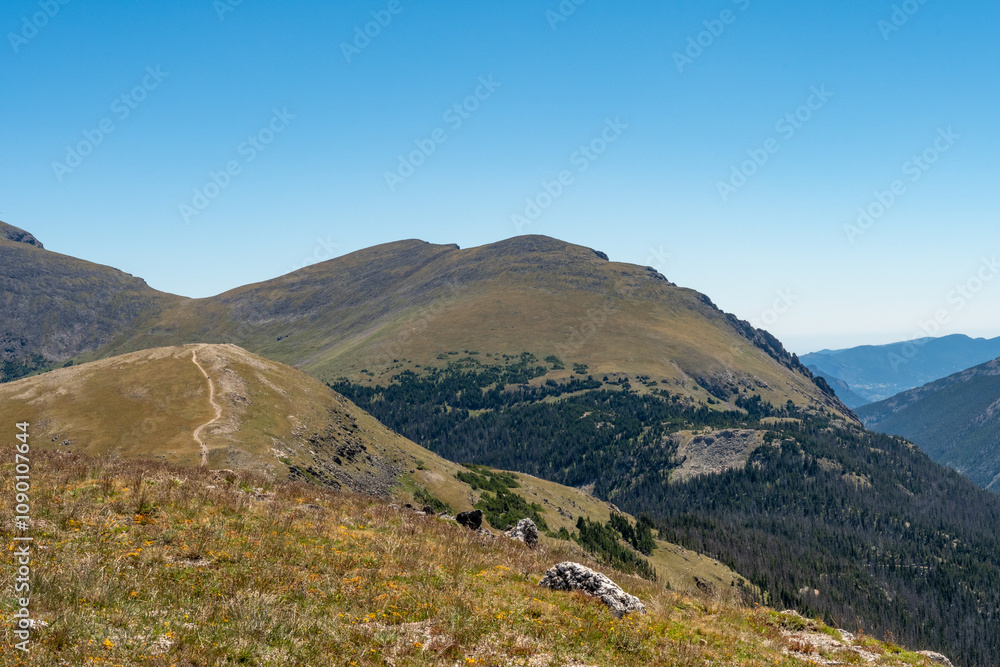 Fototapeta premium Vast mountain landscape showcasing rolling hills and clear blue sky during a bright summer day in the wilderness