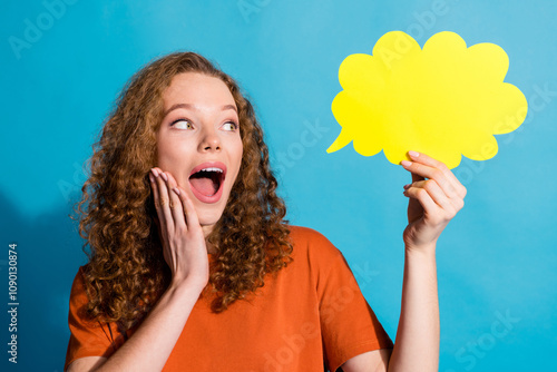 Photo of red hair girl with curls in orange t shirt hold paper bubble touch cheek surprised great idea isolated on blue color background photo