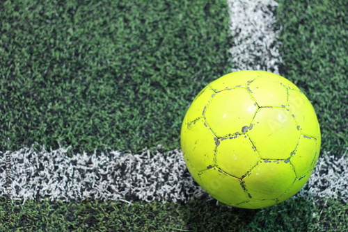 Close-up of a bright yellow soccer ball positioned between field lines on green grass, viewed from above. A vibrant scene ready for the game to start photo