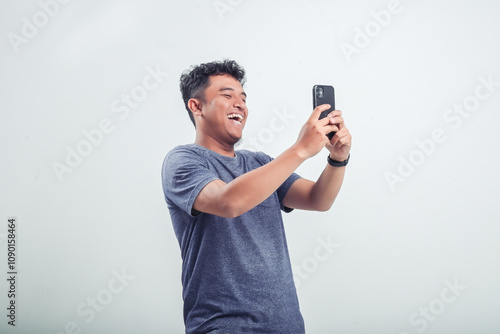 Adult Asian man laughing out loud while holding and looking at smartphone screen photo