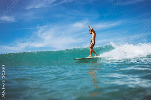 A man is surfing on a wave in the ocean. The water is blue and the sky is clear