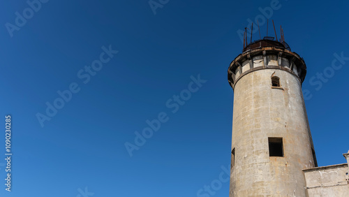 A fragment of an old lighthouse. A tall dilapidated cylindrical tower against a clear blue sky. Open dark window openings. Mauritius.  Île aux Fouquets   photo