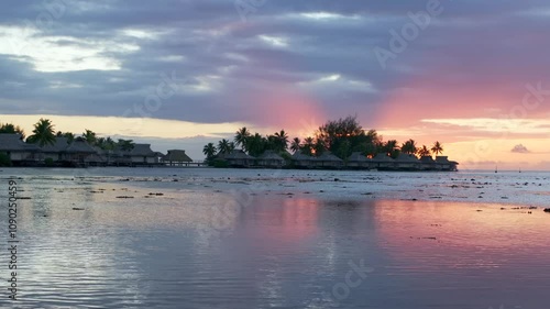 Stunning vibrant pink orange sunset Bungalow villas islands Cooks Opunohu Bay Moorea French Polynesia aerial drone clouds lagoon coral reef Pacific Ocean low tide beach slow slide right pan up motion photo