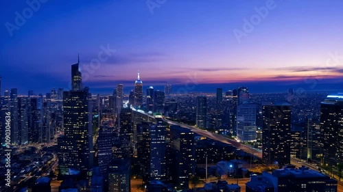 Wallpaper Mural Dusk settles over a sprawling city skyline, highlighting towering buildings and busy roadways bathed in purple and blue hues. The atmosphere merges energy with tranquility as night begins. Torontodigital.ca