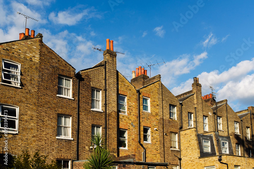 Photography Terraced brick houses with chimneys and antennas under blue sky in london