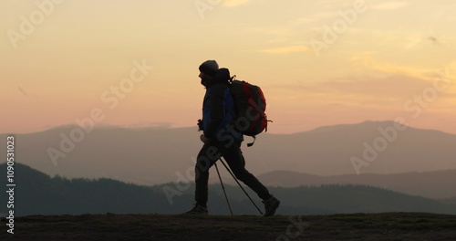 Silhouette of a traveler walking on a mountain slope against the background of majestic mountains. The evening light emphasizes his figure, creating an atmosphere of adventure and the search for new h photo