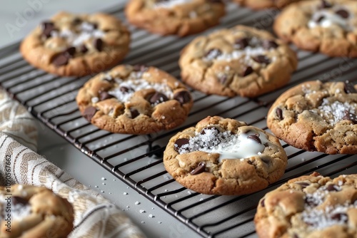 A cooling rack holds several delicious, goldenbrown chocolate chip cookies topped with sea salt.