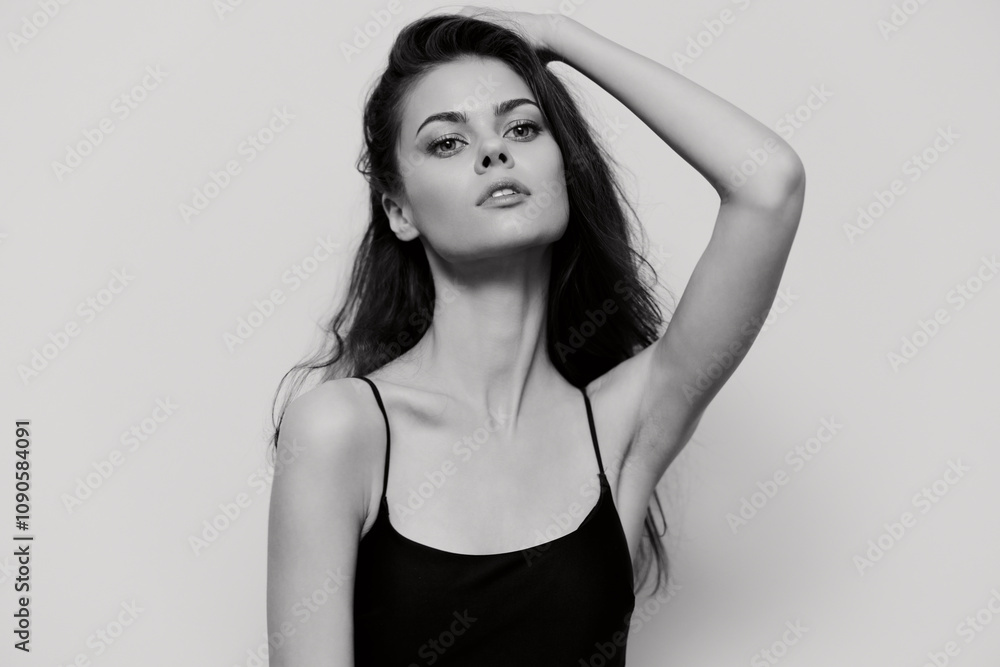 Fototapeta premium Elegant young woman posing confidently with one hand on her head, showcasing beauty and grace in a minimalist black and white setting. Fashion and portrait concept.