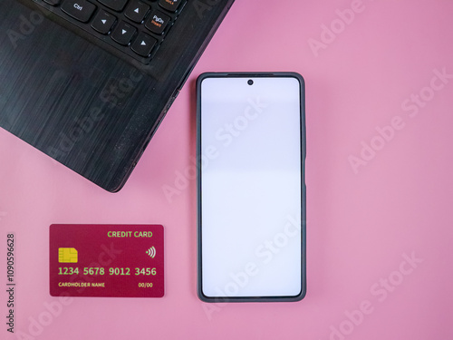 Credit cards, smartphone with blank screen and laptop on a pink background, representing technology and finance photo